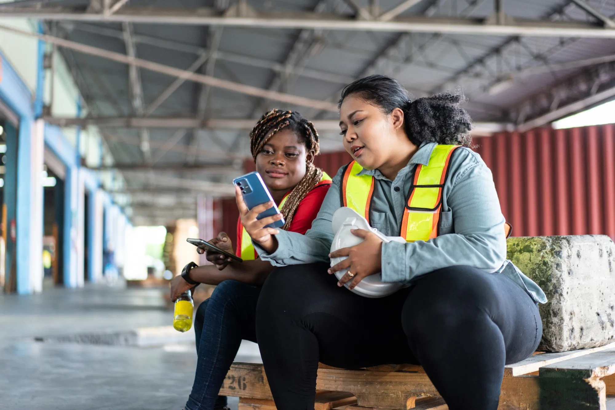 Two warehouse workers in hi-vis checking their phones on a break